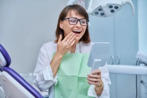woman looking at her teeth through a hand mirror in dental office