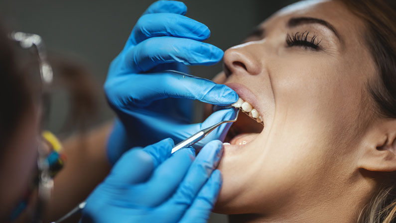 The beautiful young woman is at the dentist. She sits in the dentist's chair and the dentist sets braces on her teeth putting aesthetic self-aligning lingual locks.