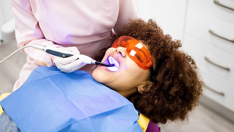 An adult woman with Arabian features visits a dentist's clinic.The doctor uses a curing or light-curing lamp to harden dental material.Dental filling in dark-skinned women.