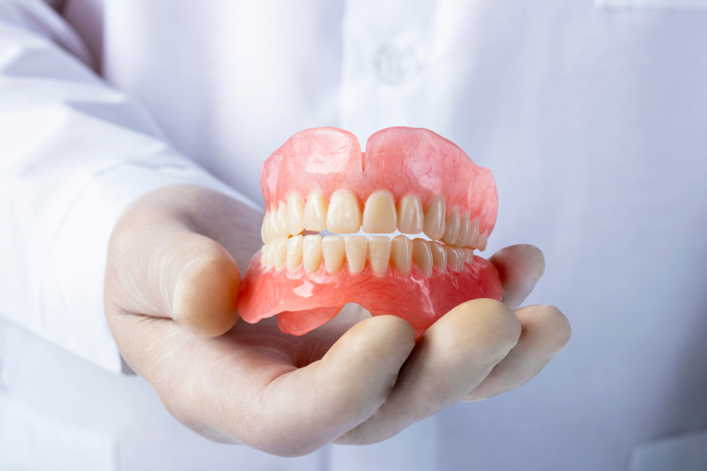 Hand of a Dentist with gloves holding a false teeth prosthesis.